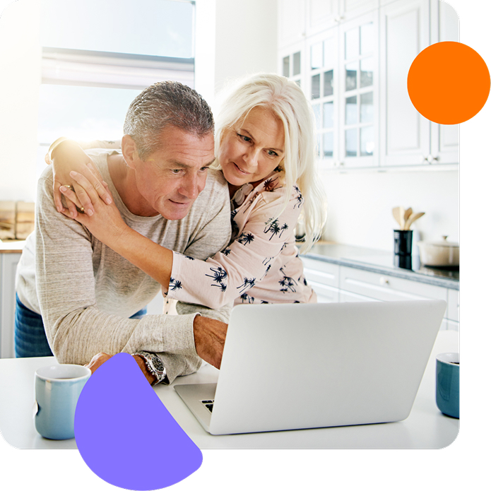 Mature couple in a bright kitchen looking at a laptop together, with the woman hugging the man from behind, surrounded by colorful abstract shapes.